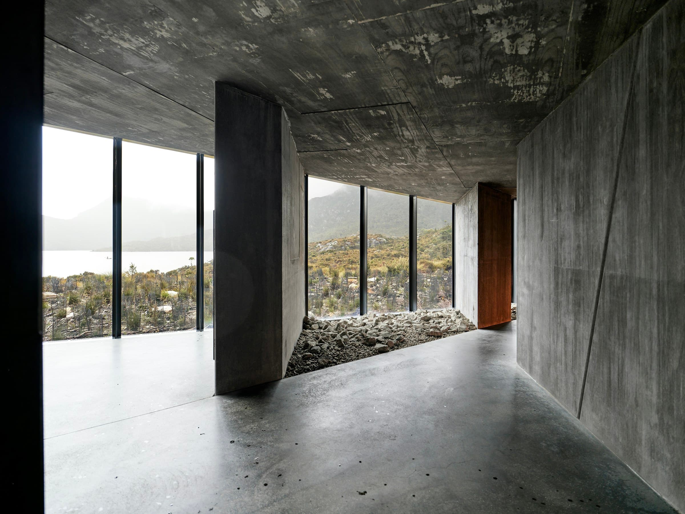 Reduziertes Betoninterieur mit raumhohen Fenstern und Blick in die Landschaft